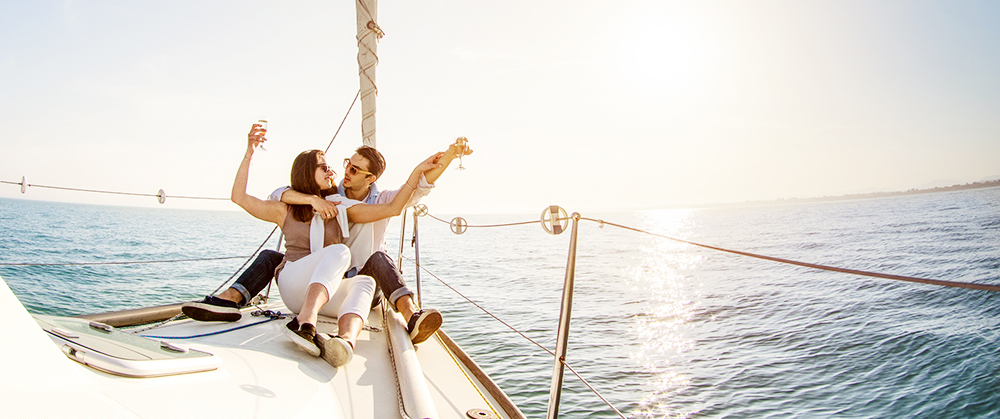 Young couple in love on sail boat with champagne at sunset - Happy people lifestyle on exclusive luxury concept  - Soft backlight focus on warm afternoon sunshine filter - Fisheye lens distortion