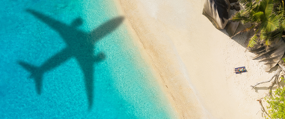 Concept of airplane travel to exotic destination with shadow of commercial airplane flying above beautiful tropical beach. Beach holidays and travel.